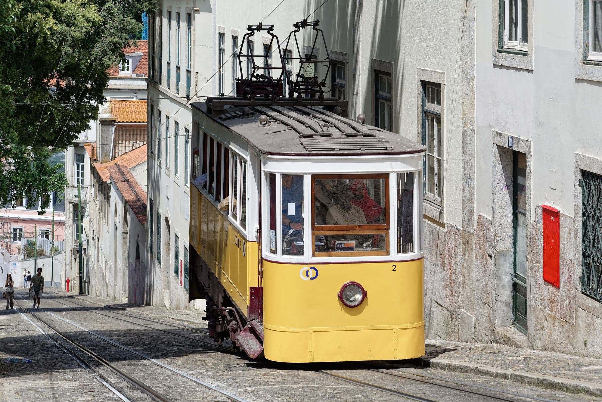 A yellow funicular car climbing a steep cobbled street between pale buildings.