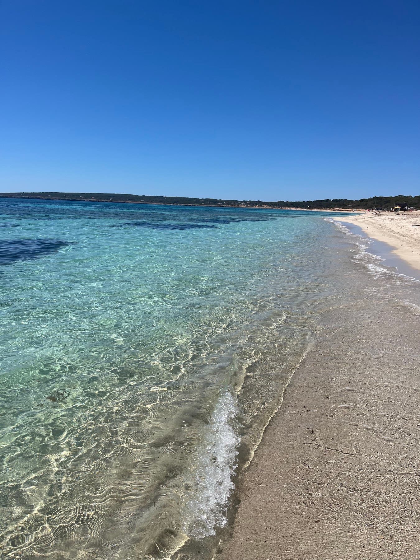 Clear shallow water along an empty sandy beach.